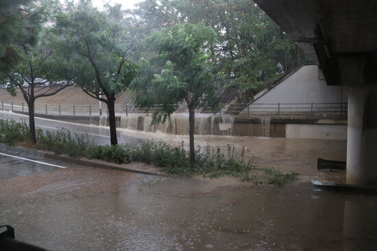 Un rierol format per l'acumulació d'aigua de pluja que desemboca en un pas que creua les vies.