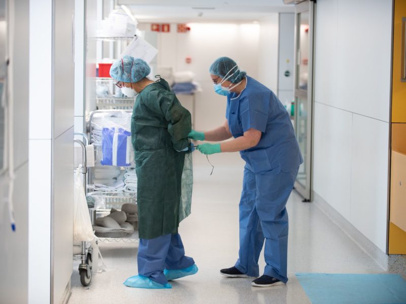 Una professional sanitària corda a una companya una bata abans d'atendre un pacient amb covid-19. Foto: ACN.